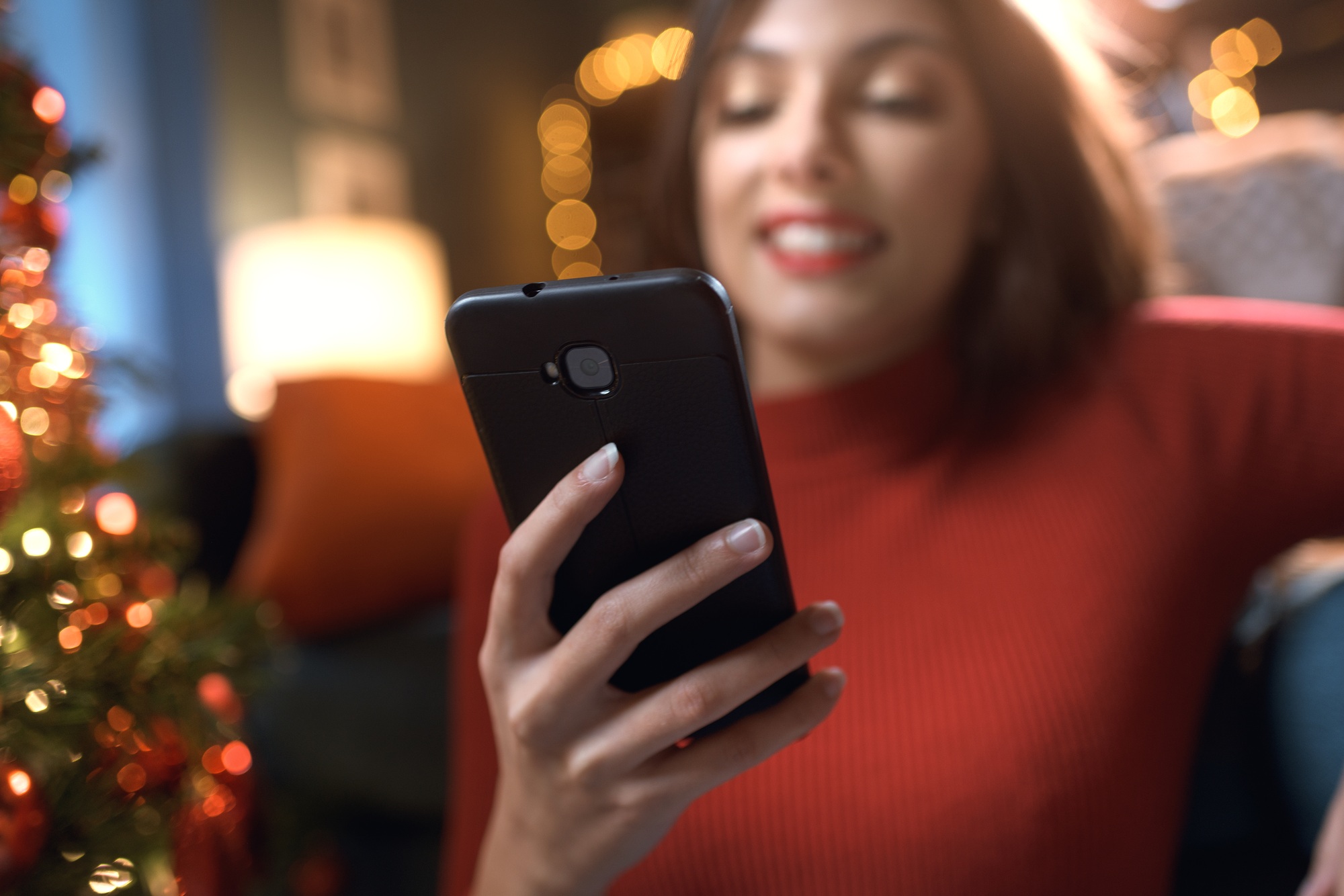 Smiling woman sending Christmas wishes with her smartphone